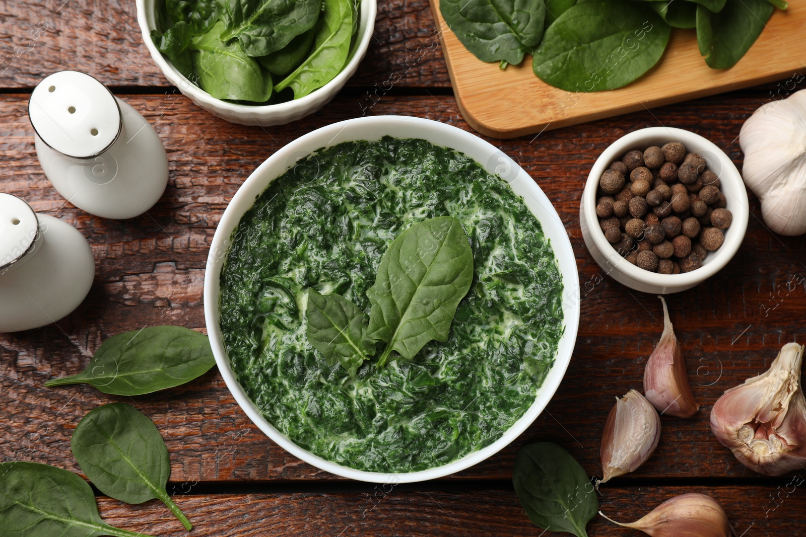 Photo of Delicious spinach sauce in bowl and spices on wooden table, flat lay