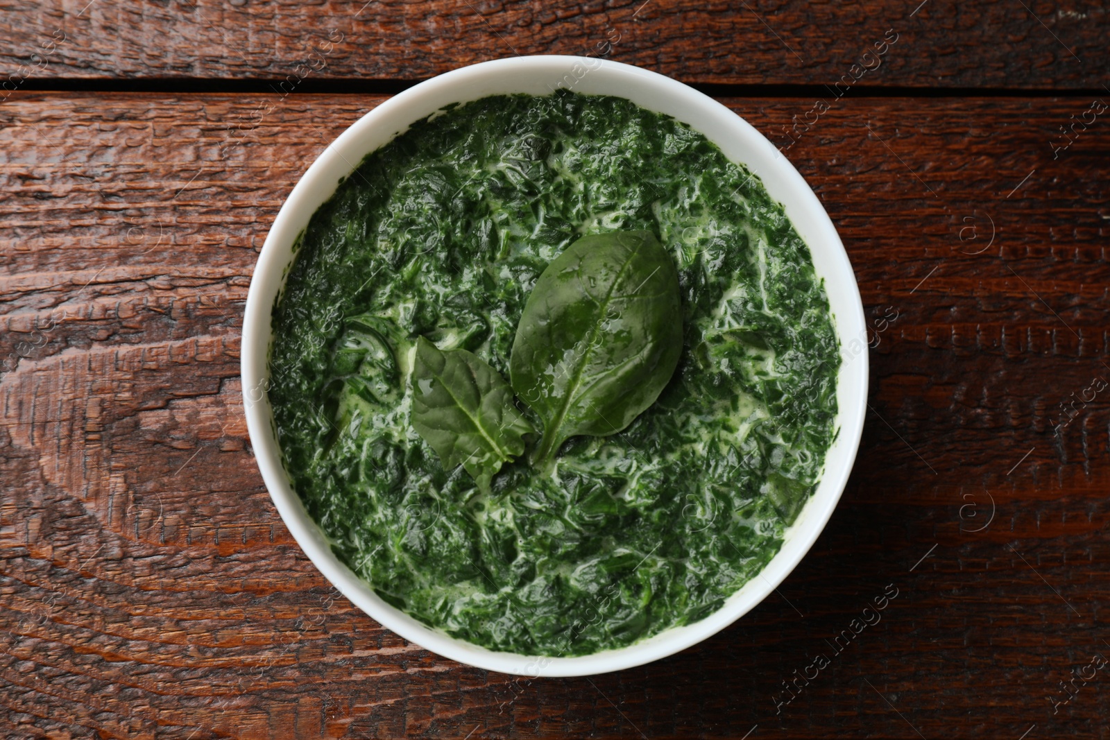 Photo of Delicious spinach sauce in bowl on wooden table, top view