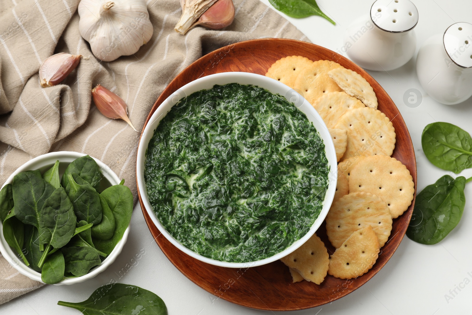 Photo of Delicious spinach sauce in bowl, crackers and garlic on white marble table, flat lay