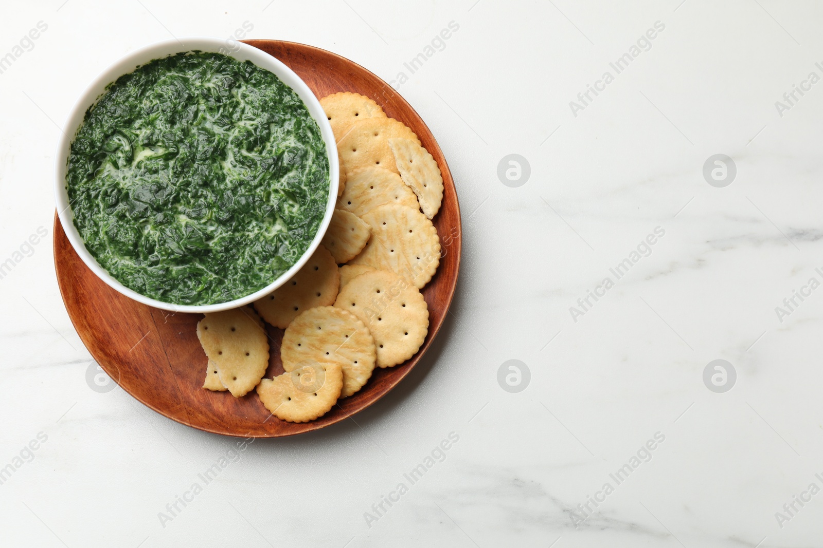 Photo of Delicious spinach sauce in bowl and crackers on white marble table, top view. Space for text