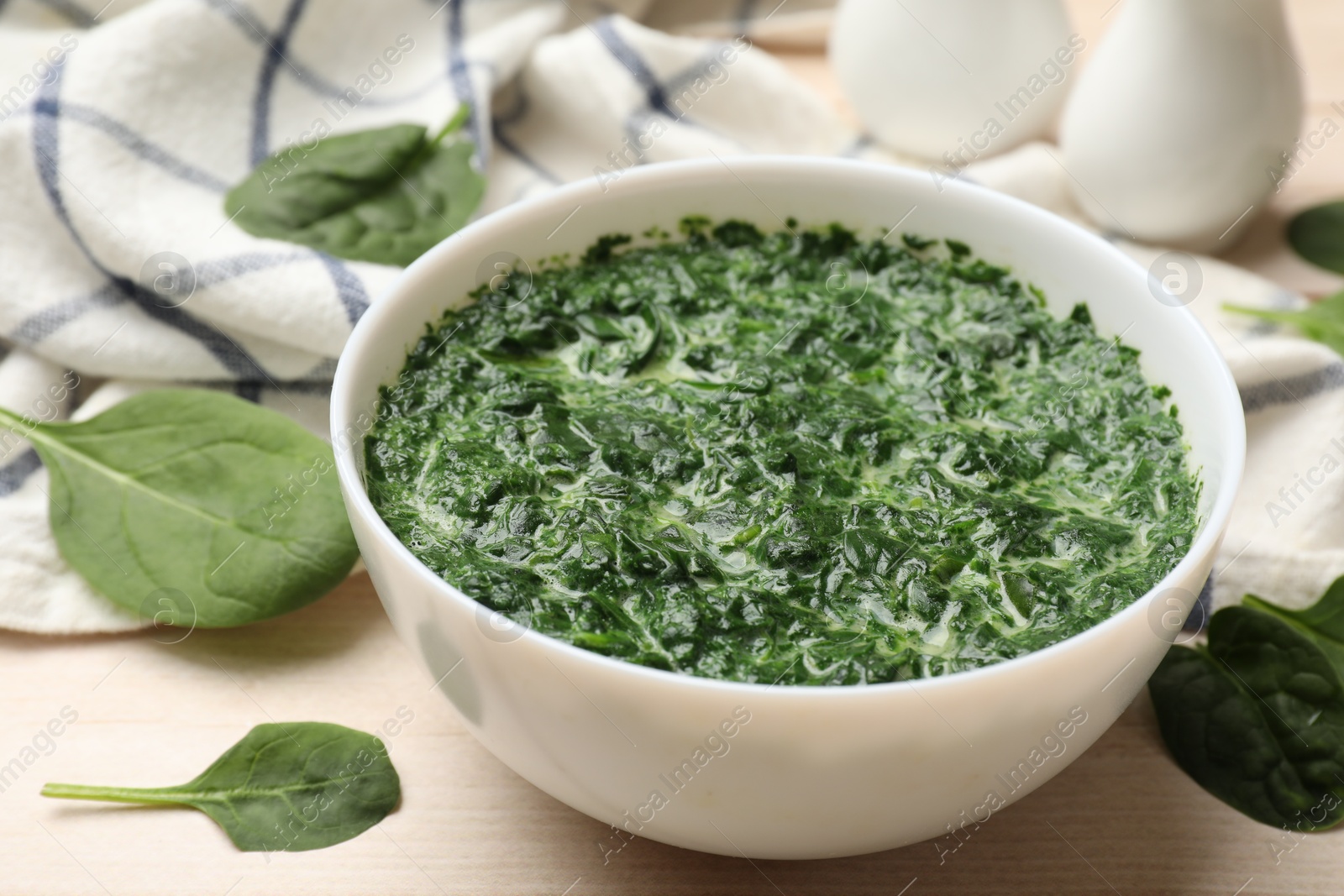 Photo of Delicious spinach sauce in bowl and leaves on wooden table, closeup