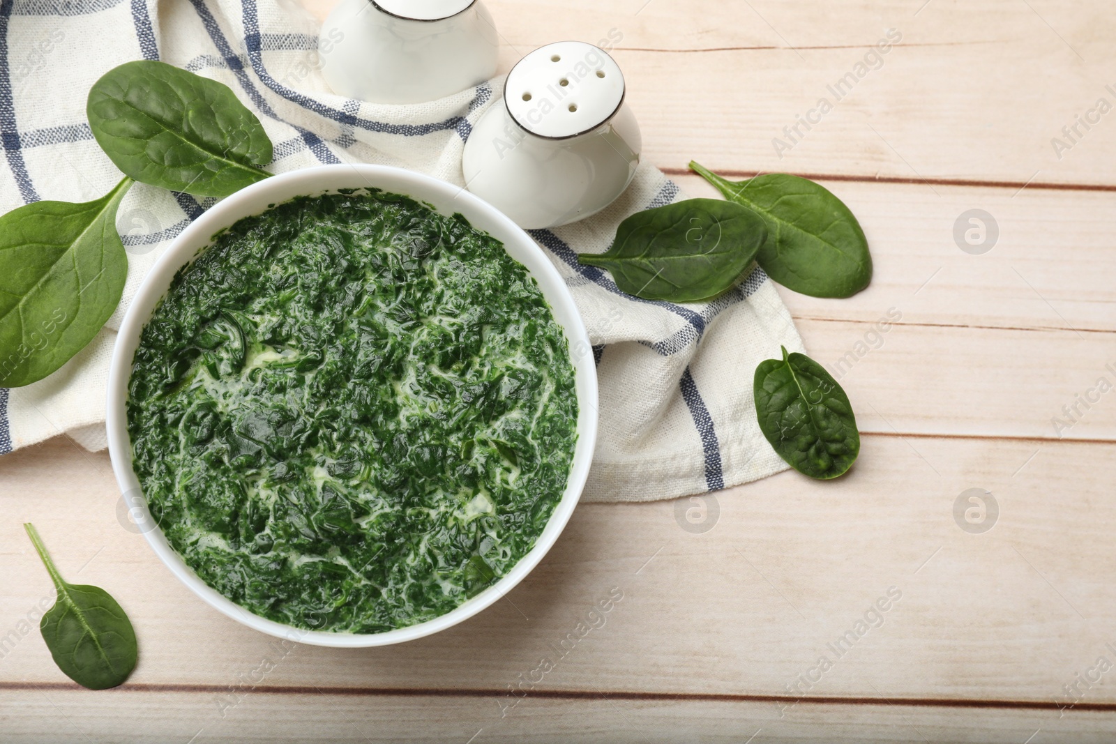 Photo of Delicious spinach sauce in bowl and leaves on wooden table, flat lay. Space for text