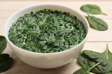 Photo of Delicious spinach sauce in bowl and leaves on wooden table, closeup