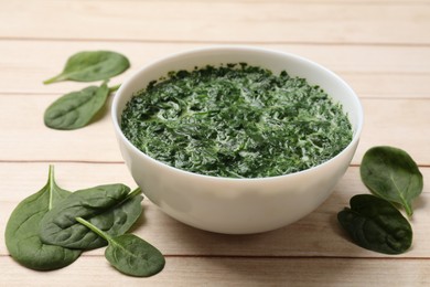 Photo of Delicious spinach sauce in bowl and leaves on wooden table, closeup