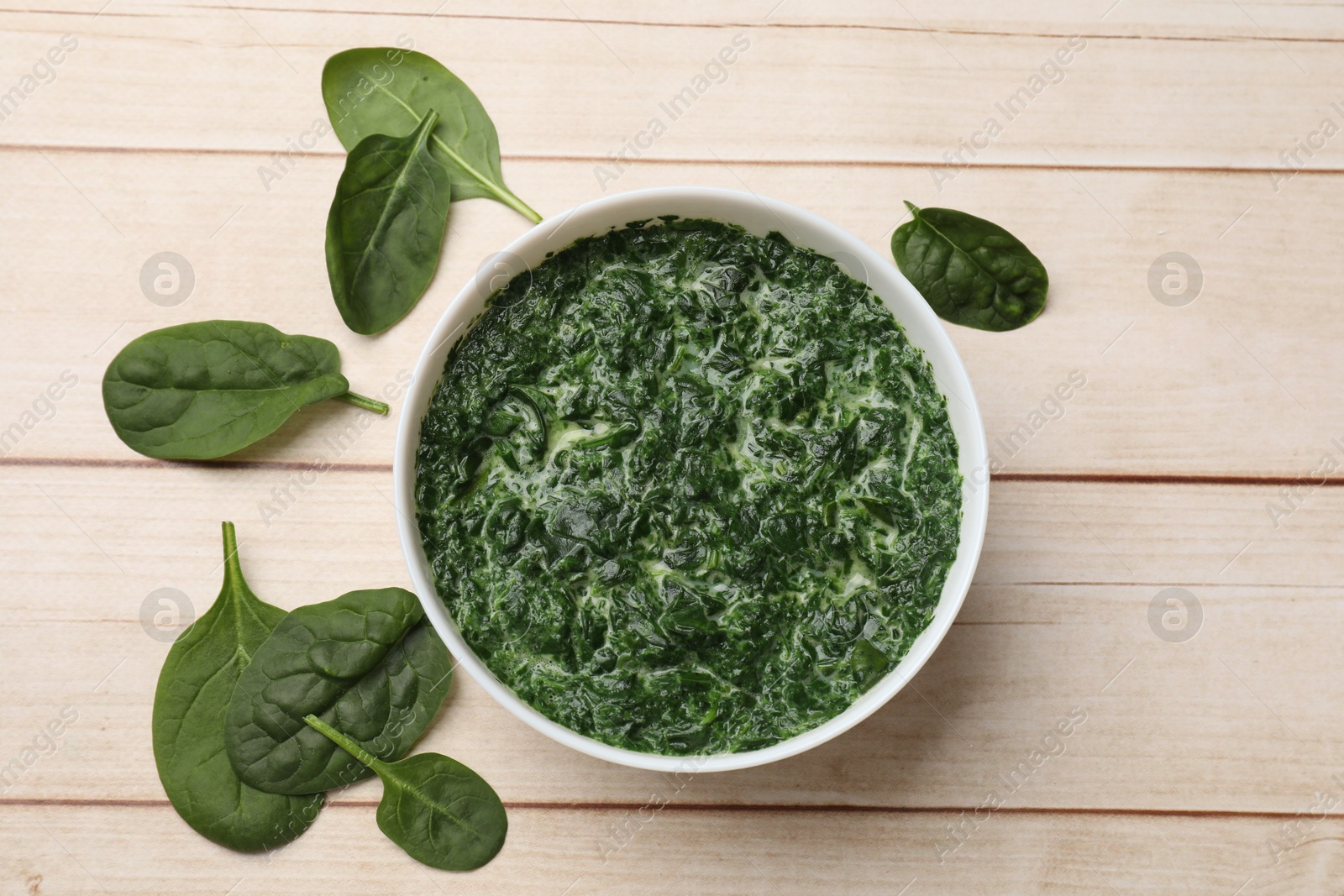 Photo of Delicious spinach sauce in bowl and leaves on wooden table, flat lay