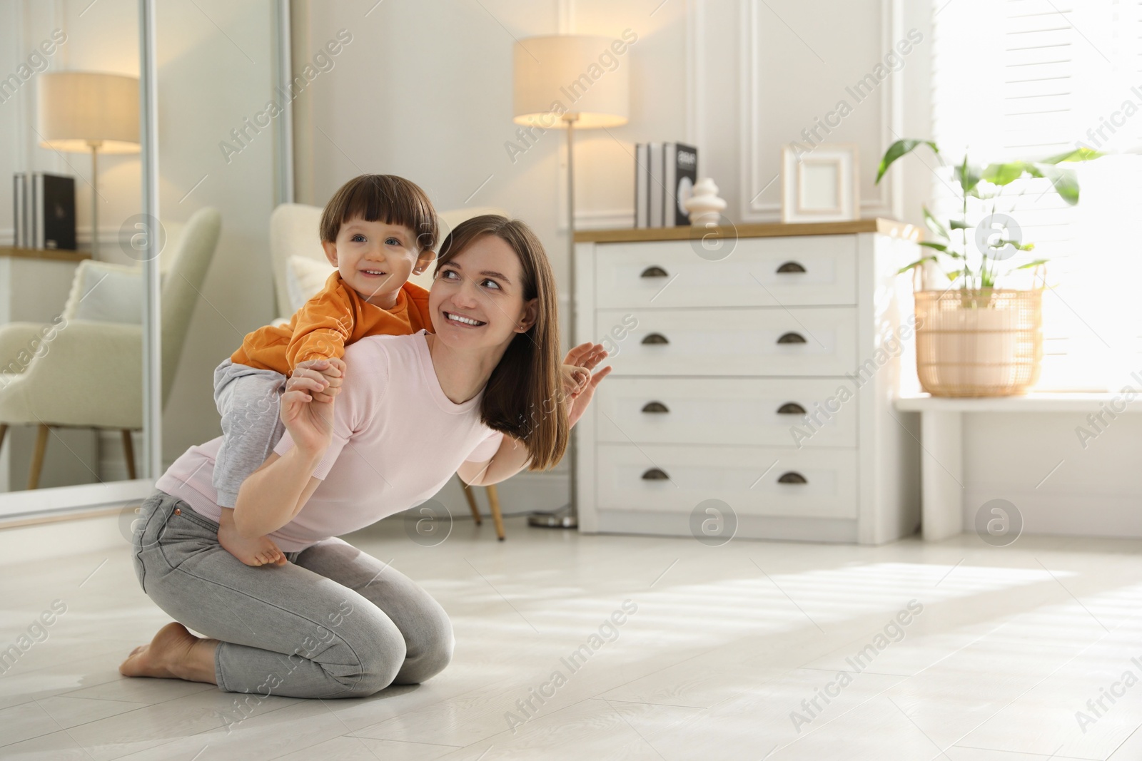 Photo of Happy mother playing with her little son at home. Space for text