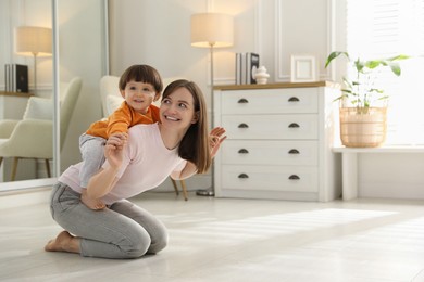 Photo of Happy mother playing with her little son at home. Space for text