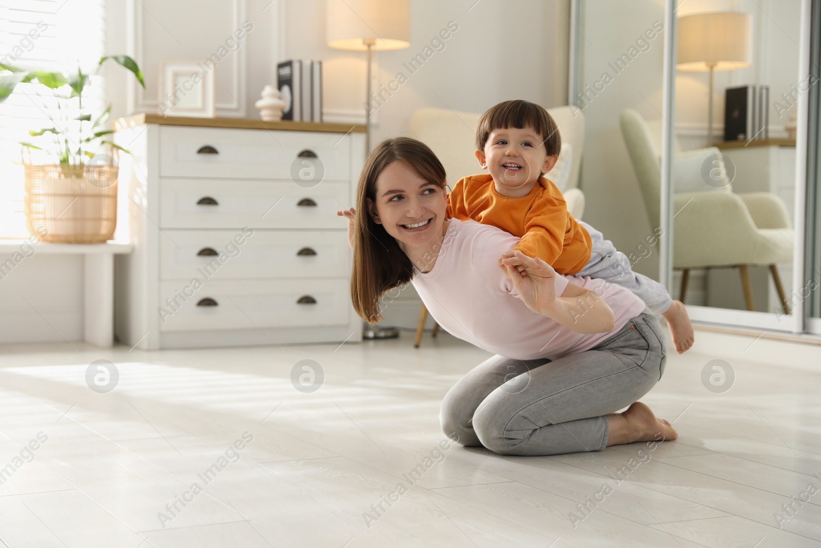 Photo of Happy mother playing with her little son at home. Space for text