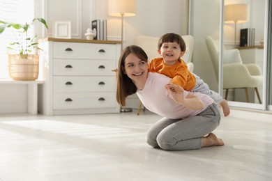 Photo of Happy mother playing with her little son at home. Space for text