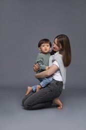 Photo of Mother hugging her little son on grey background. Space for text