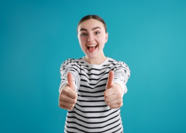 Happy woman showing thumbs up on light blue background, selective focus. Like gesture