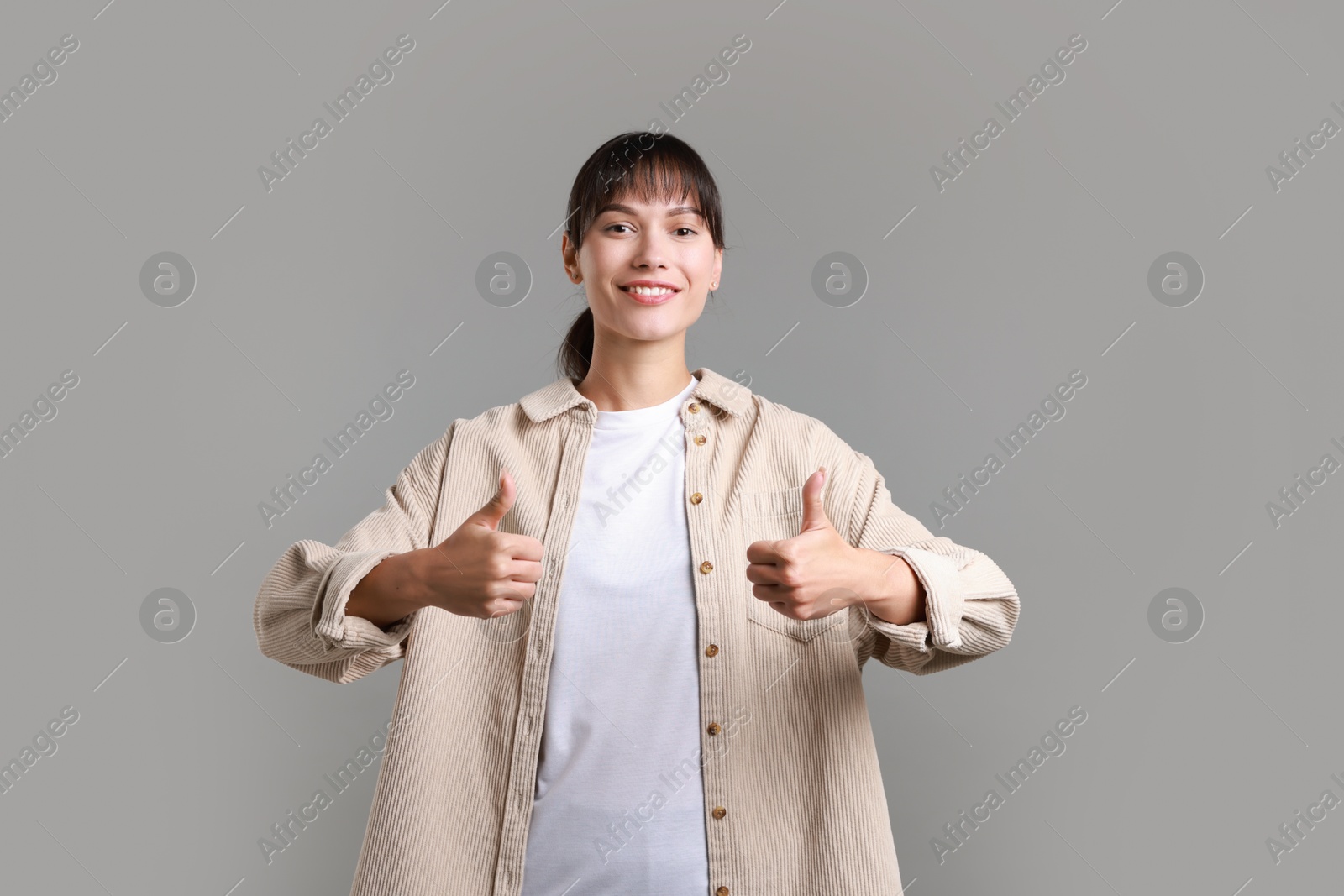 Photo of Happy woman showing thumbs up on grey background. Like gesture