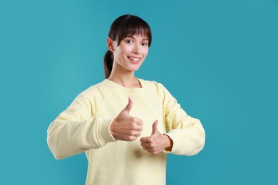 Photo of Happy woman showing thumbs up on light blue background. Like gesture