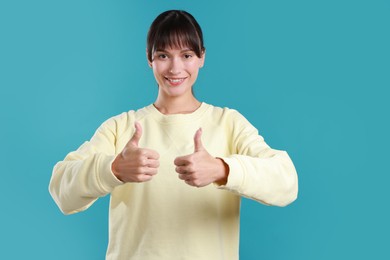 Photo of Happy woman showing thumbs up on light blue background. Like gesture