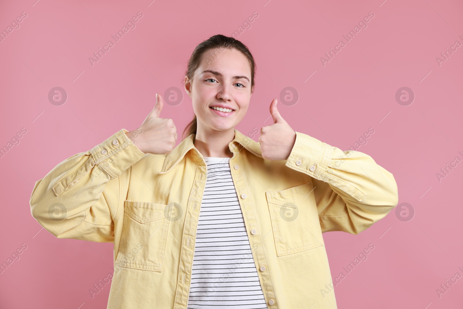 Photo of Happy woman showing thumbs up on pink background. Like gesture