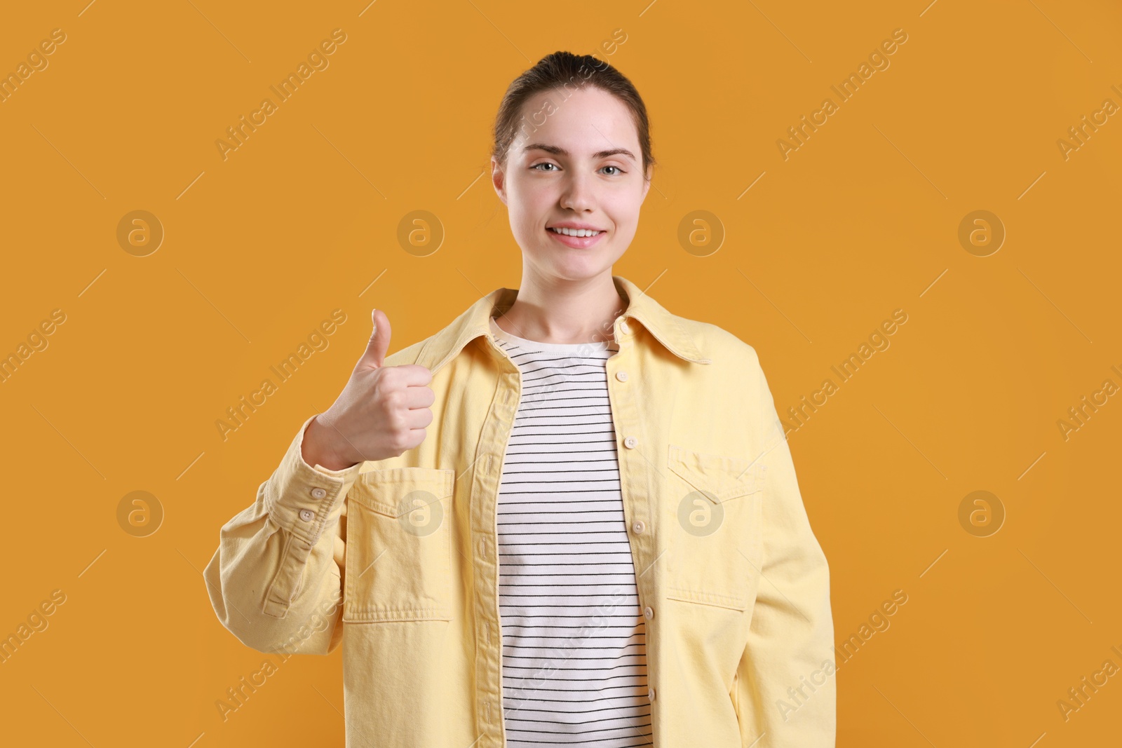 Photo of Happy woman showing thumbs up on orange background. Like gesture