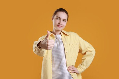 Photo of Woman showing thumbs up on orange background. Like gesture