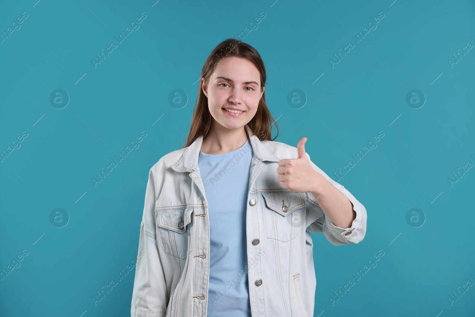 Photo of Happy woman showing thumbs up on light blue background. Like gesture