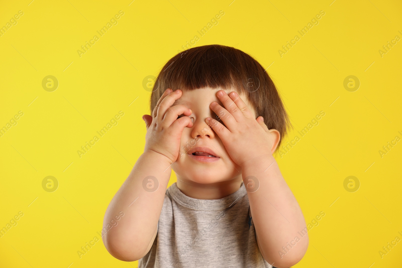 Photo of Cute little boy covering eyes on yellow background