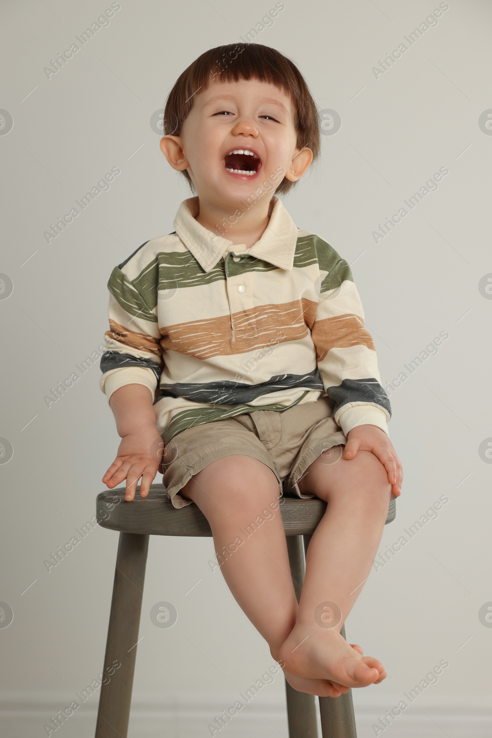 Photo of Emotional little boy sitting on stool against light grey background