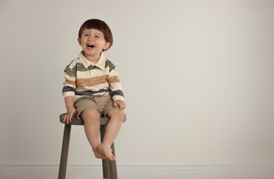 Photo of Emotional little boy sitting on stool against light grey background. Space for text