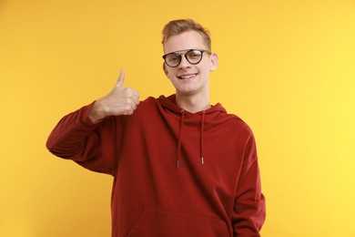 Photo of Happy man showing thumbs up on yellow background. Like gesture