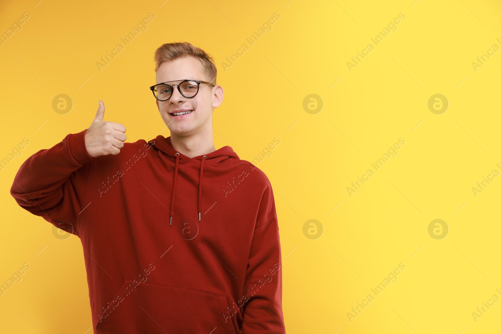 Photo of Happy man showing thumbs up on yellow background, space for text. Like gesture