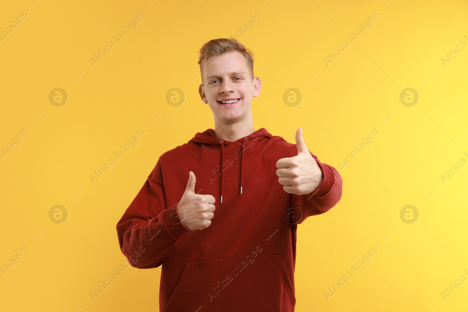 Photo of Happy man showing thumbs up on yellow background. Like gesture