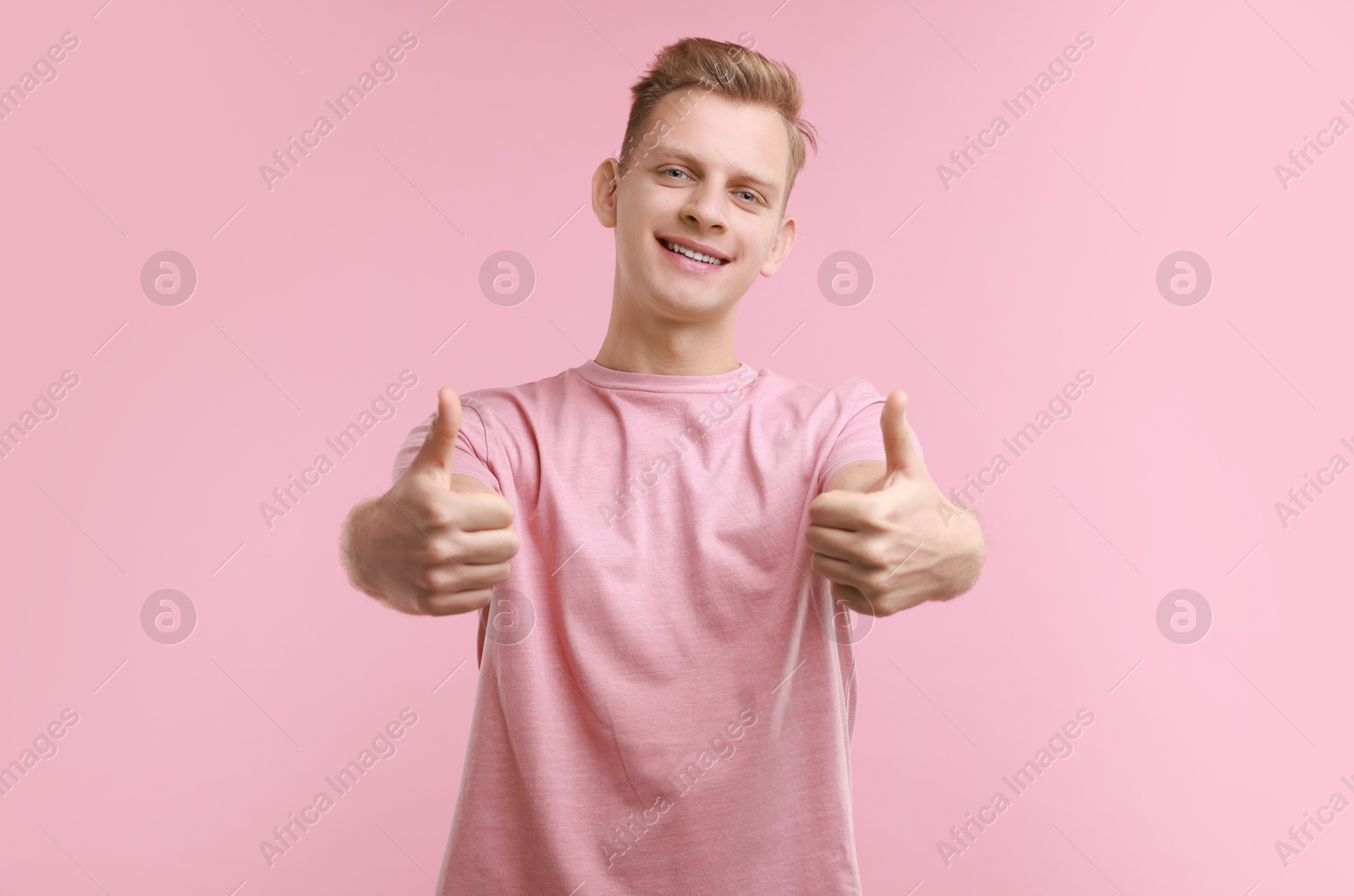 Photo of Happy man showing thumbs up on pink background. Like gesture