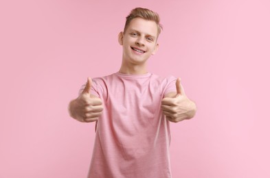 Photo of Happy man showing thumbs up on pink background. Like gesture