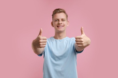 Photo of Happy man showing thumbs up on pink background. Like gesture