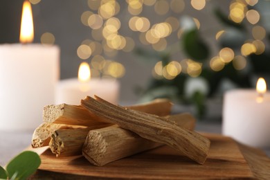 Photo of Palo santo sticks and burning candles on table, closeup