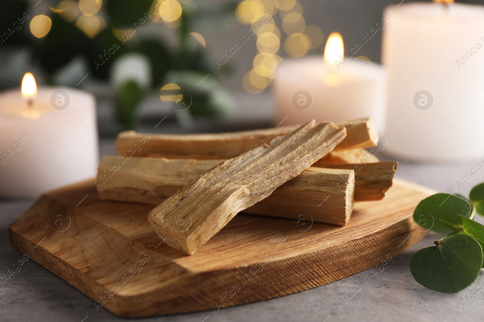 Photo of Palo santo sticks, eucalyptus leaves and burning candles on grey table, closeup