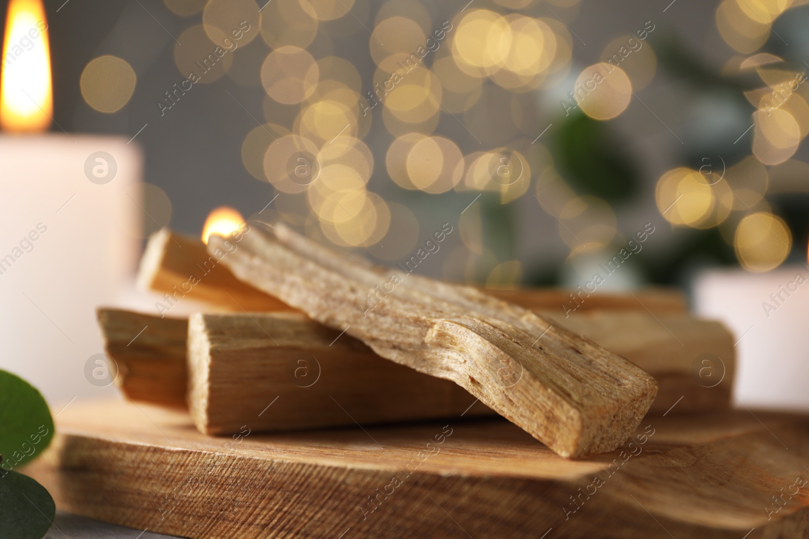 Photo of Palo santo sticks and burning candle on table, closeup