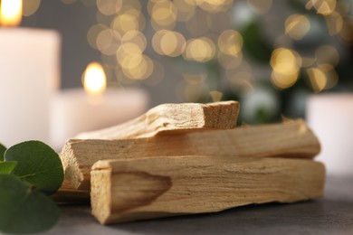 Photo of Palo santo sticks, eucalyptus branch and burning candles on grey table, closeup