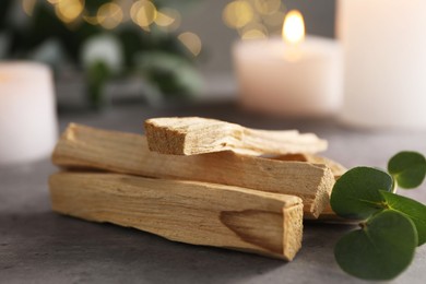 Photo of Palo santo sticks, eucalyptus branch and burning candles on grey table, closeup