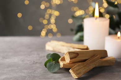 Photo of Palo santo sticks, eucalyptus branch and burning candles on grey table, closeup. Space for text