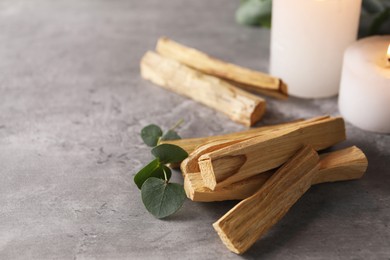 Photo of Palo santo sticks, eucalyptus branch and burning candles on grey table, closeup. Space for text