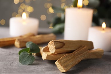 Photo of Palo santo sticks, eucalyptus branch and burning candles on grey table, closeup