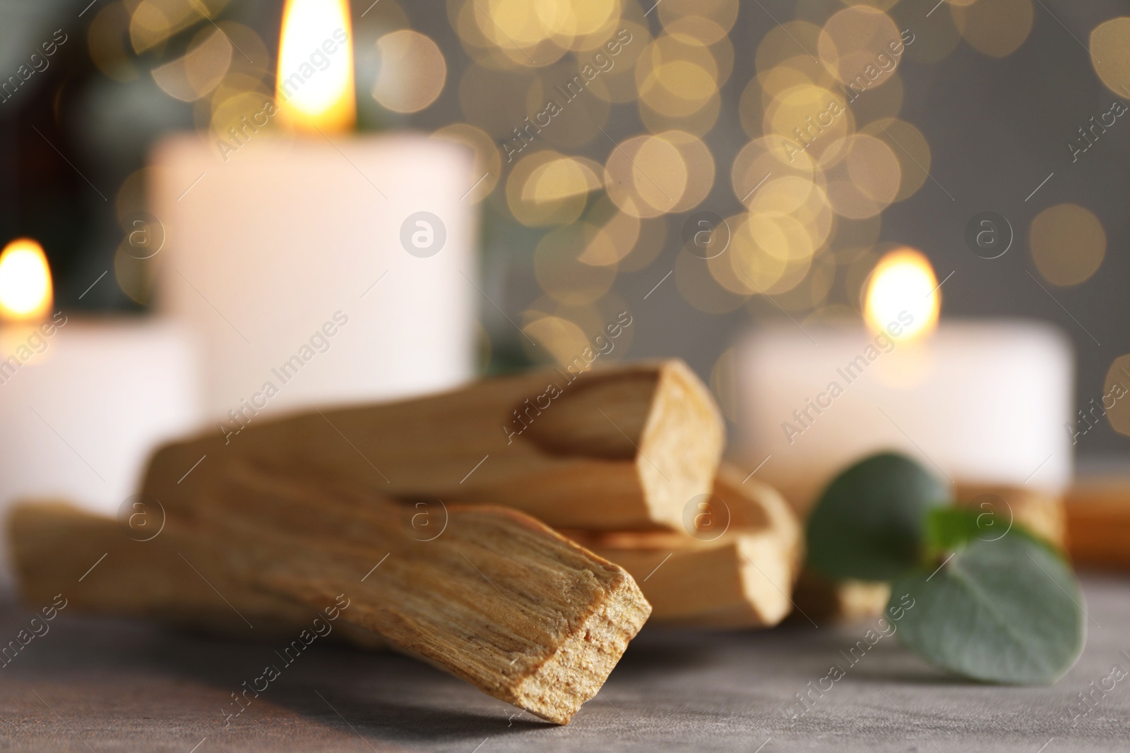 Photo of Palo santo sticks, eucalyptus branch and burning candles on grey table, closeup