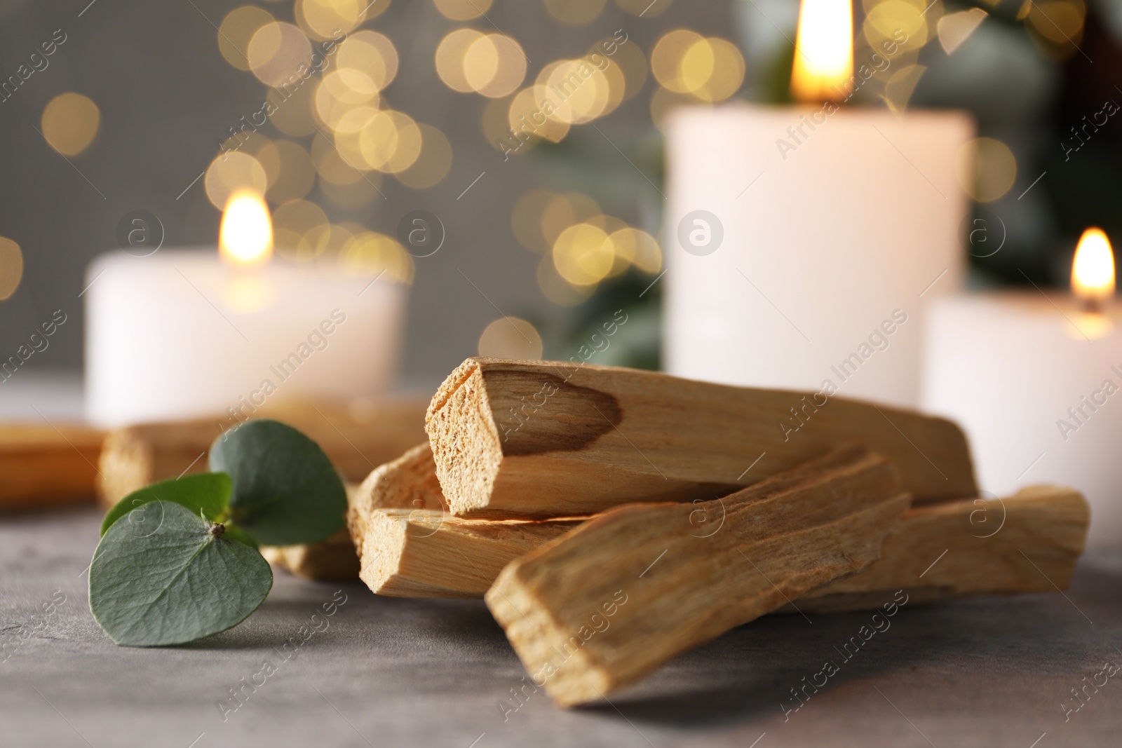 Photo of Palo santo sticks, eucalyptus branch and burning candles on grey table, closeup