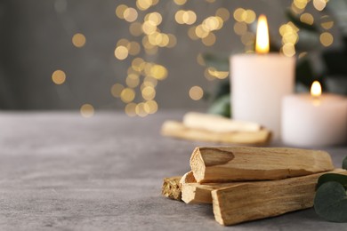 Photo of Palo santo sticks, eucalyptus branch and burning candles on grey table, closeup. Space for text