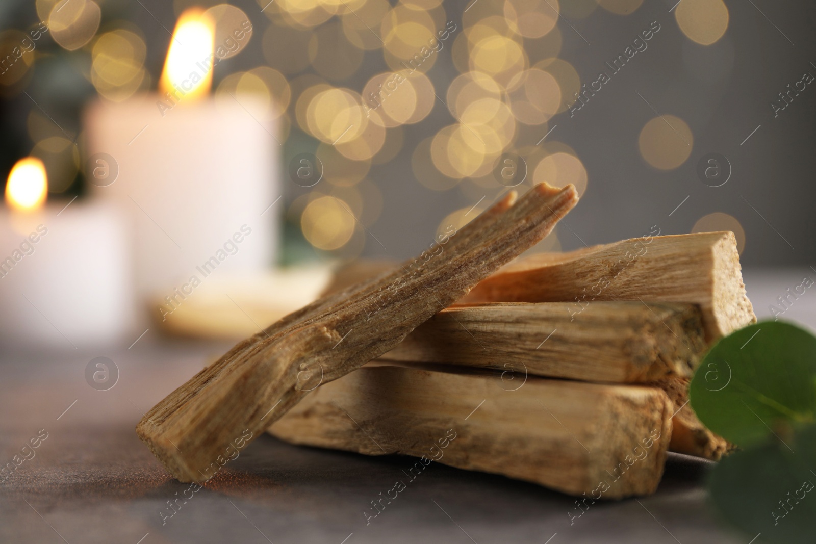 Photo of Palo santo sticks, eucalyptus leaves and burning candles on grey table, closeup