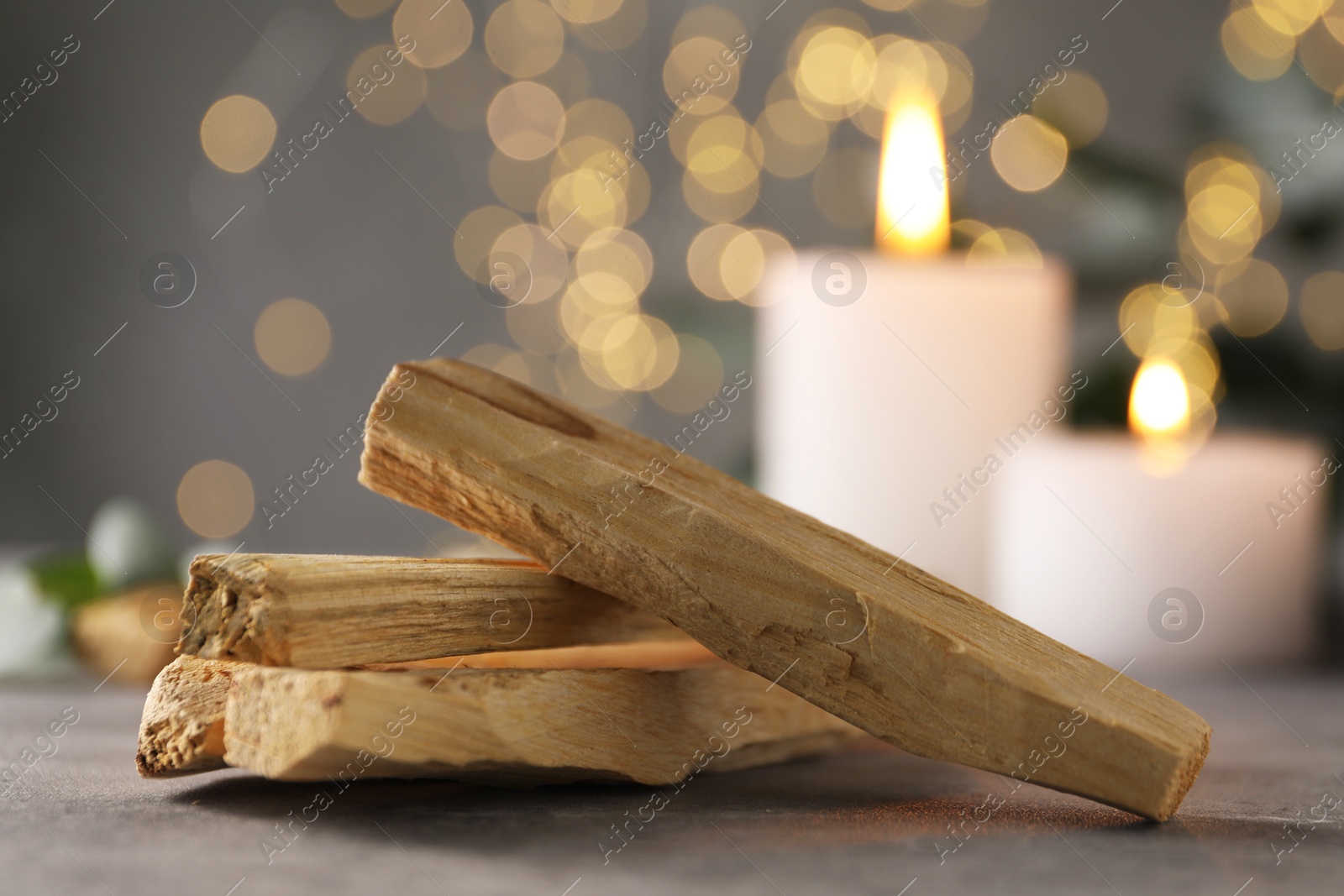 Photo of Palo santo sticks and burning candles on grey table, closeup