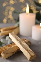 Photo of Palo santo sticks and burning candles on grey table, closeup