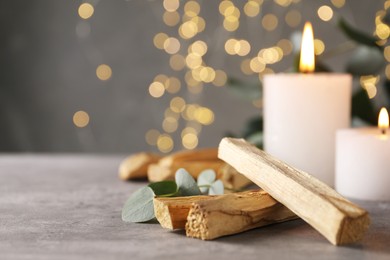 Photo of Palo santo sticks, eucalyptus branch and burning candles on grey table, closeup. Space for text