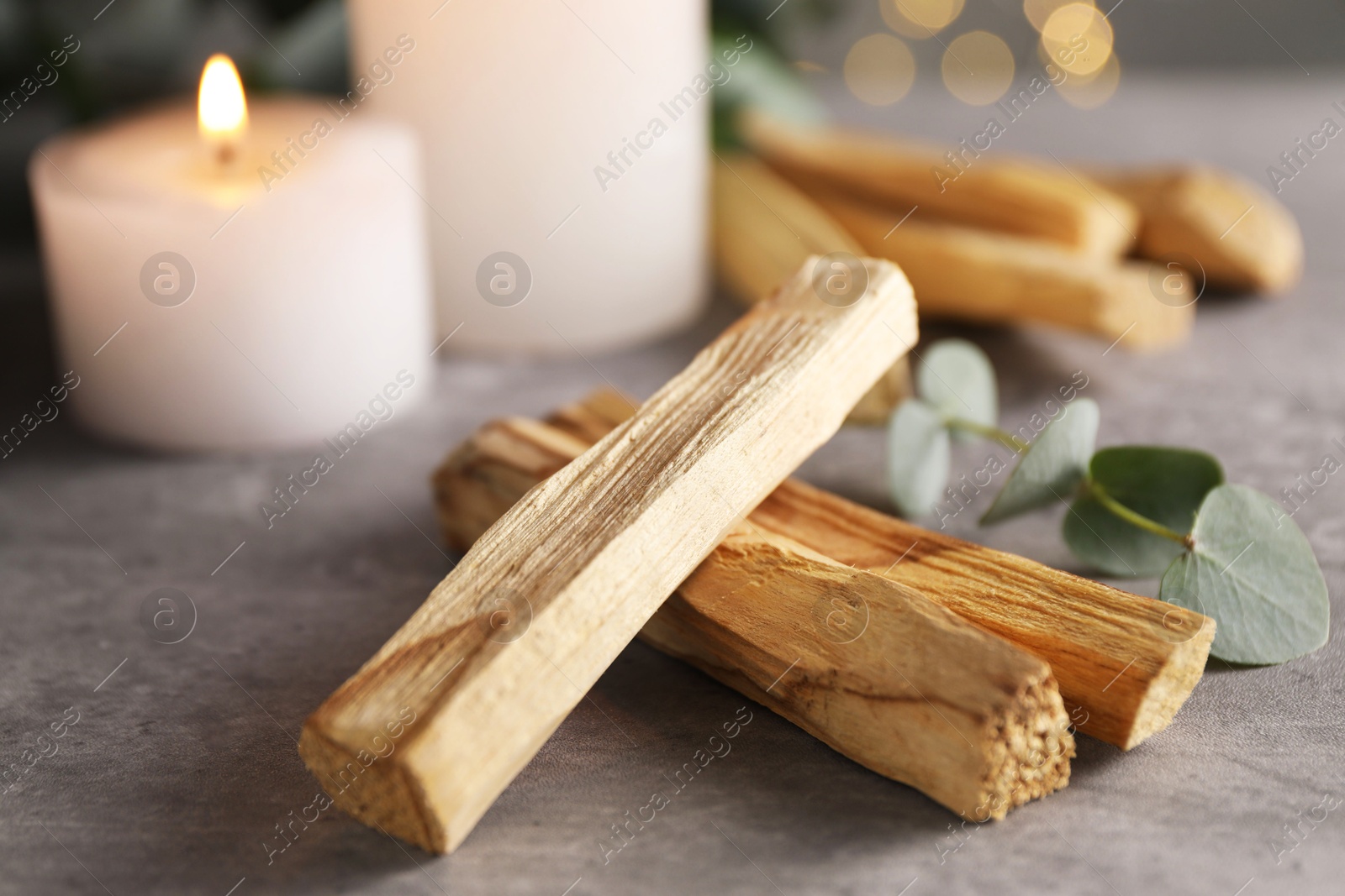 Photo of Palo santo sticks, eucalyptus branch and burning candles on grey table, closeup