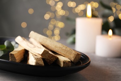 Photo of Palo santo sticks and burning candles on grey table, closeup