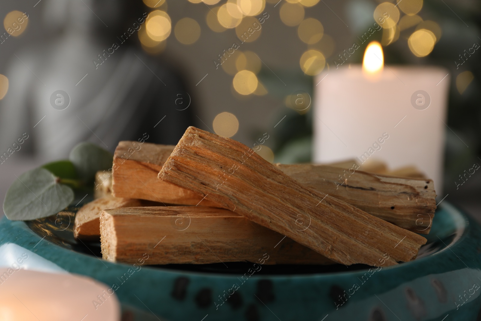 Photo of Palo santo sticks, eucalyptus leaves and burning candle on table, closeup