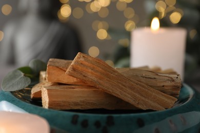 Photo of Palo santo sticks, eucalyptus leaves and burning candle on table, closeup